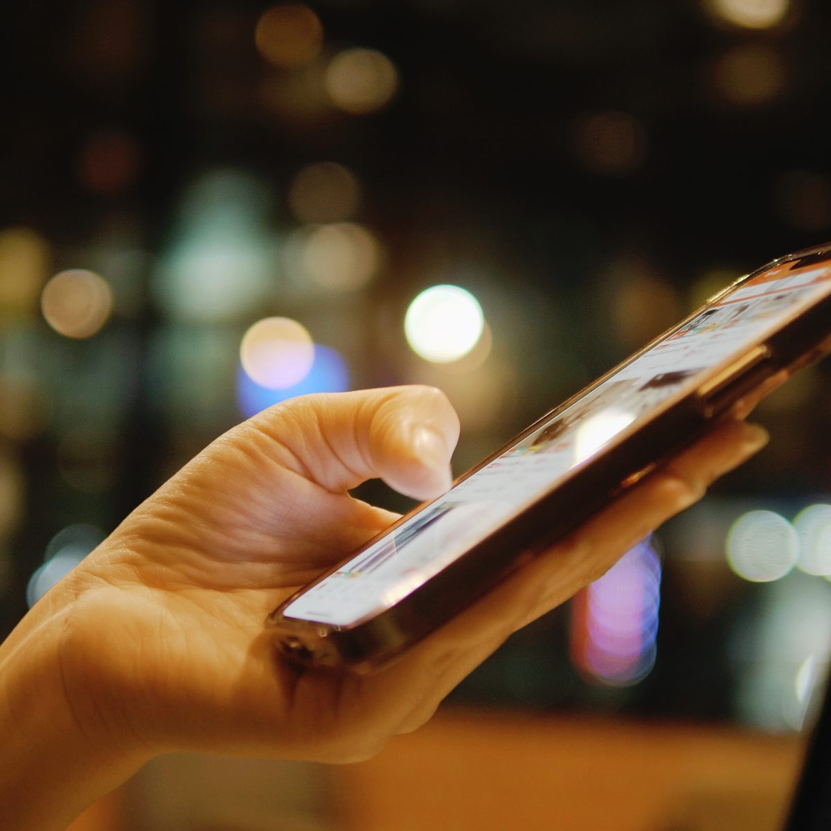 Hand scrollt abends durch Kurzvideos auf dem Smartphone